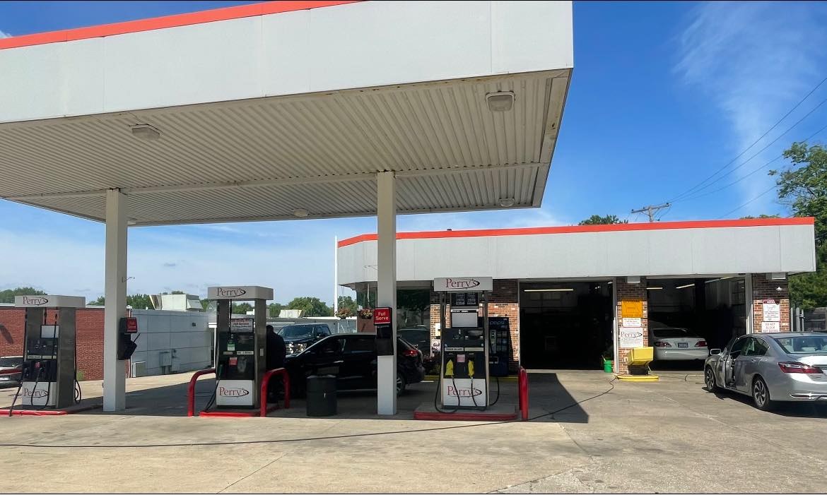 The forecourt in daylight with Perry's branded pumps under a red and white canopy and the repair bays behind
